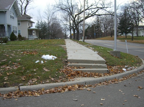 Flint Steps and a non ADA compliant curb cut in Flint, Michigan make this sidewalk impossible to use by anyone requiring a mobility device. Photo by Barbara McCann